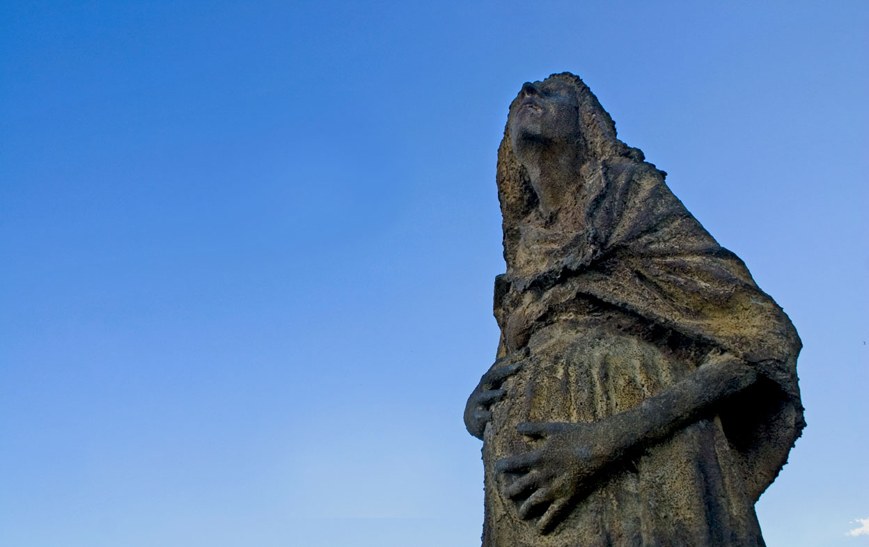 Le visage et le torse de la statue d’une femme enceinte, devant un ciel bleu d’hiver.
