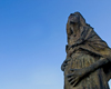 Le visage et le torse de la statue d’une femme enceinte, devant un ciel bleu d’hiver.