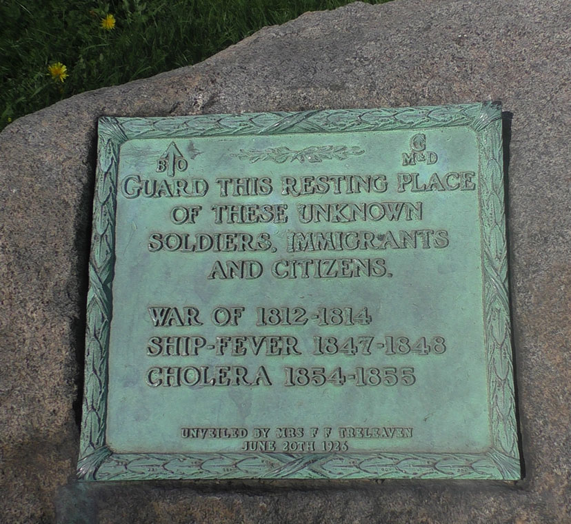 Engraved rectangular green plaque mounted on large grey stone. Green grass in background.