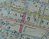 Black and white printed map, several blocks with streets coloured in red, yellow, and blue marker, proposed street extension through hospital (never carried out) indicated in purple. Open fields in centre of map.