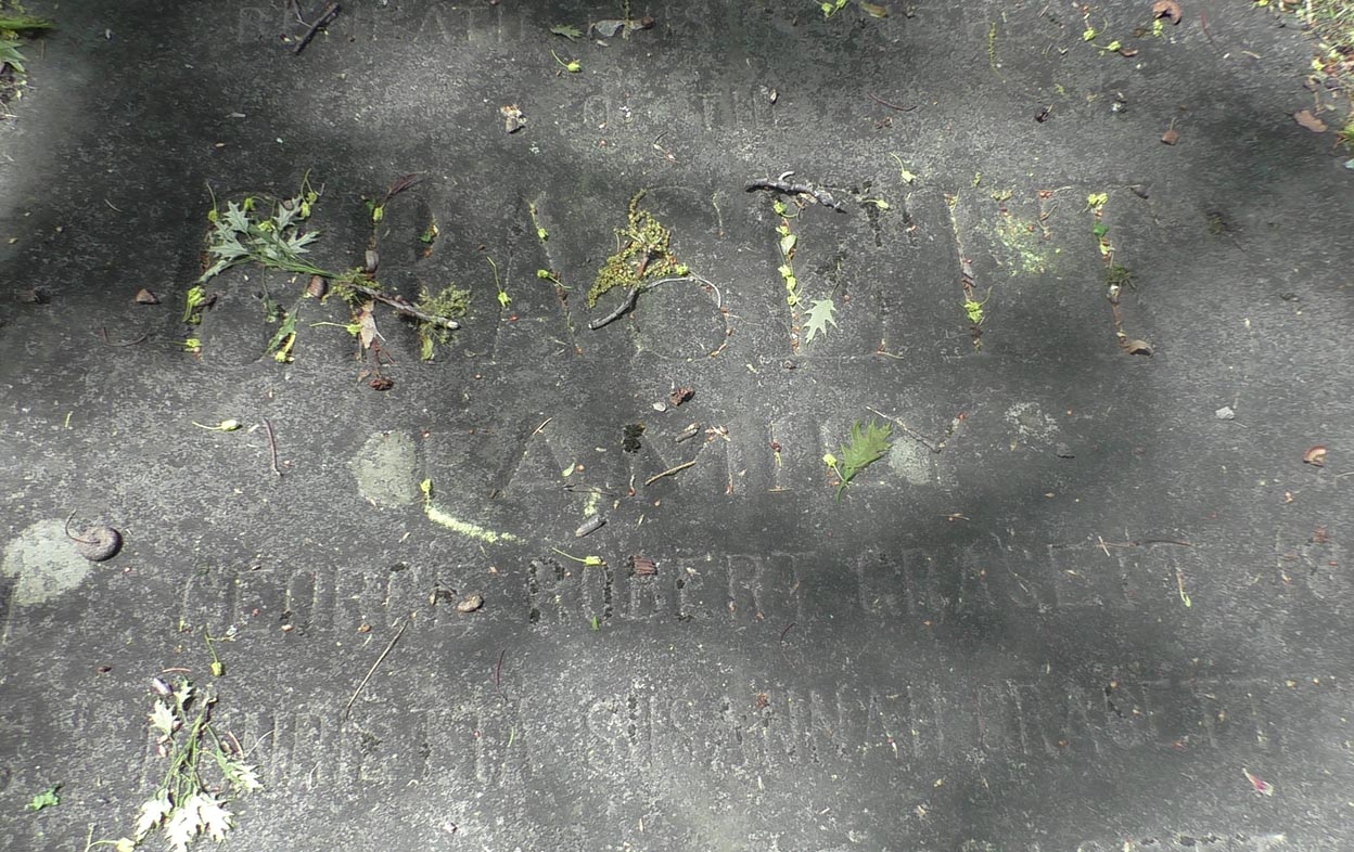 Close up photograph of horizontal grave slab with some leaves and sticks over engraving.
