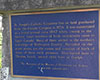 Plaque historique de couleur bleue, installée sur un socle de couleur grise et où sont gravées des notes explicatives, en caractères dorés.