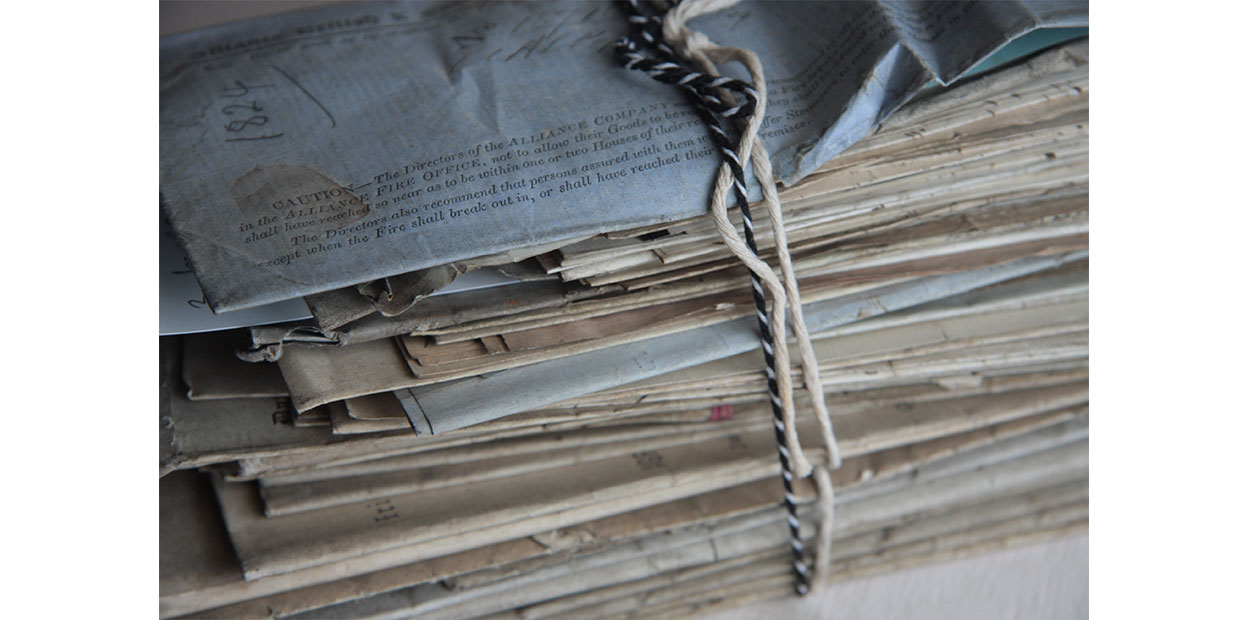 Close up photograph of a bundle of letters and documents bound together with two strands of string, one of which is white and the other blue and white. The document at the top of the bundle is dated 1824.