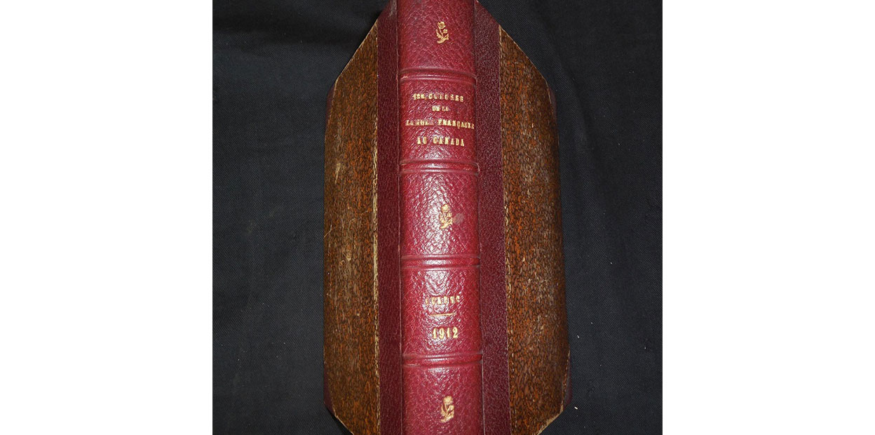 Diagonal view of red leather bound spine of book with brown covers. Premier Congrès de La Langue Français printed in gold on spine.