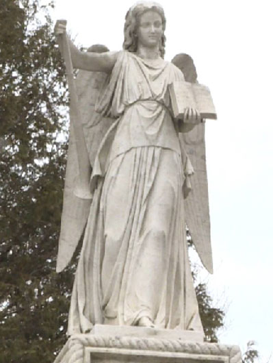 Photograph of a white sculpture of an angelic woman holding an open book standing on plinth and facing viewer.
