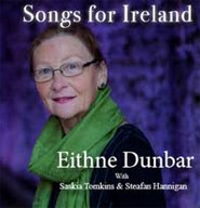 La photographie d’une dame aux cheveux foncés, portant des lunettes et un foulard vert, fixant la caméra. Un arrière-plan violet est aperçu. Les mots Songs for Ireland sont écrits au-dessus de la photographie et le nom Eithne Dunbar est inscrit au bas de l’image.