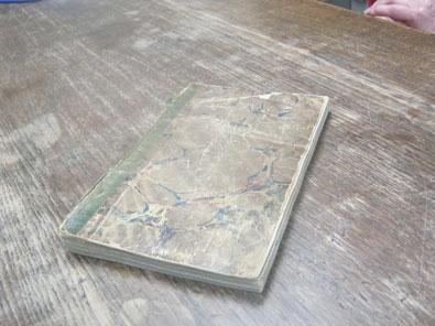 diary with fraying green binding, lying diagonally on brown table with scuffed surface.